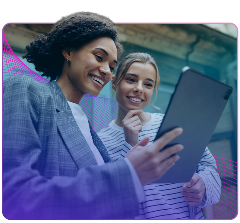 two women smiling while looking at a tablet